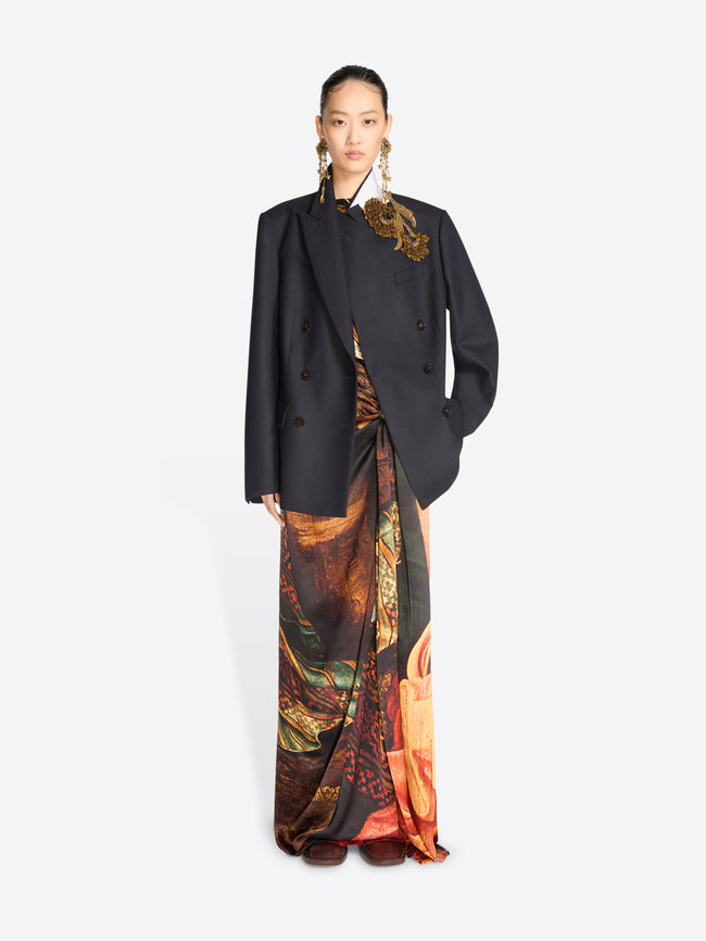 A model wearing a black double-breasted blazer over a long, wide-leg skirt with an intricate multicolor paisley and floral print.