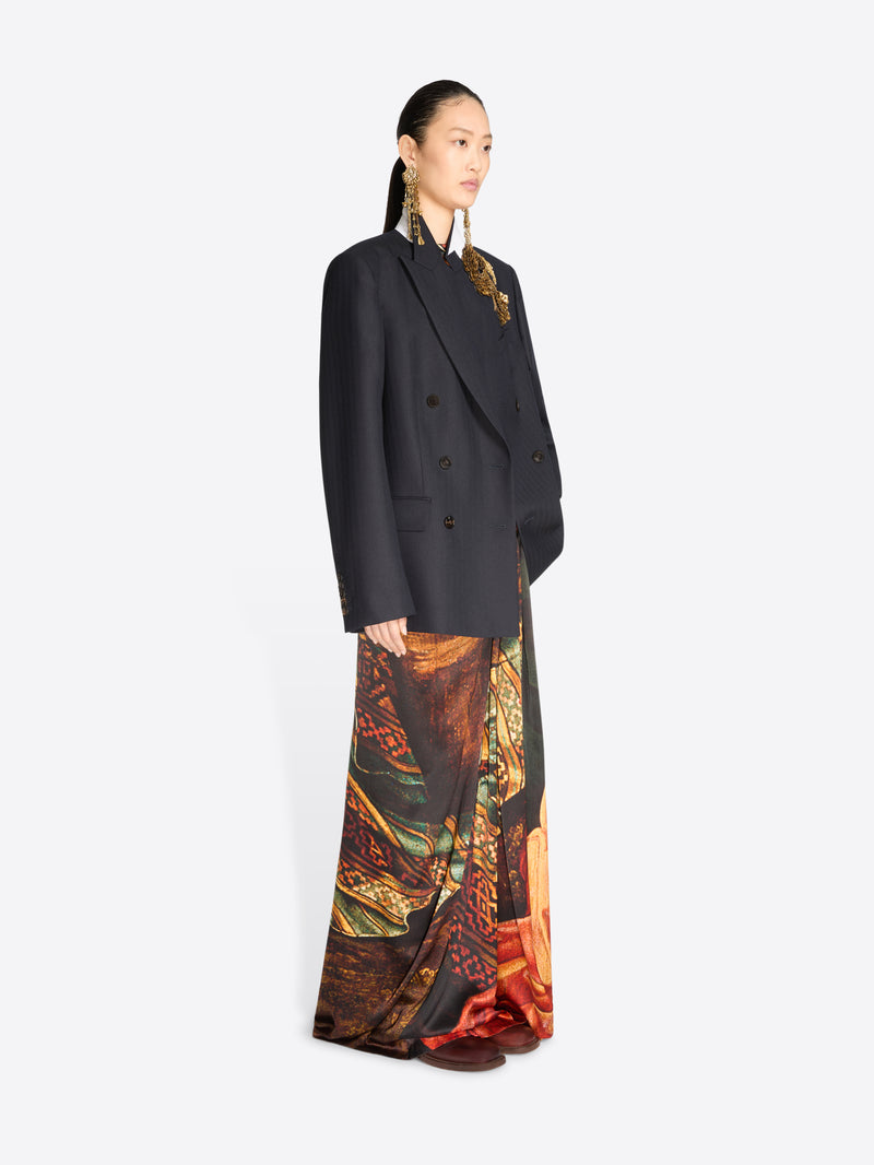 A model wearing a black double-breasted blazer over a long, wide-leg skirt with an intricate multicolor paisley and floral print.