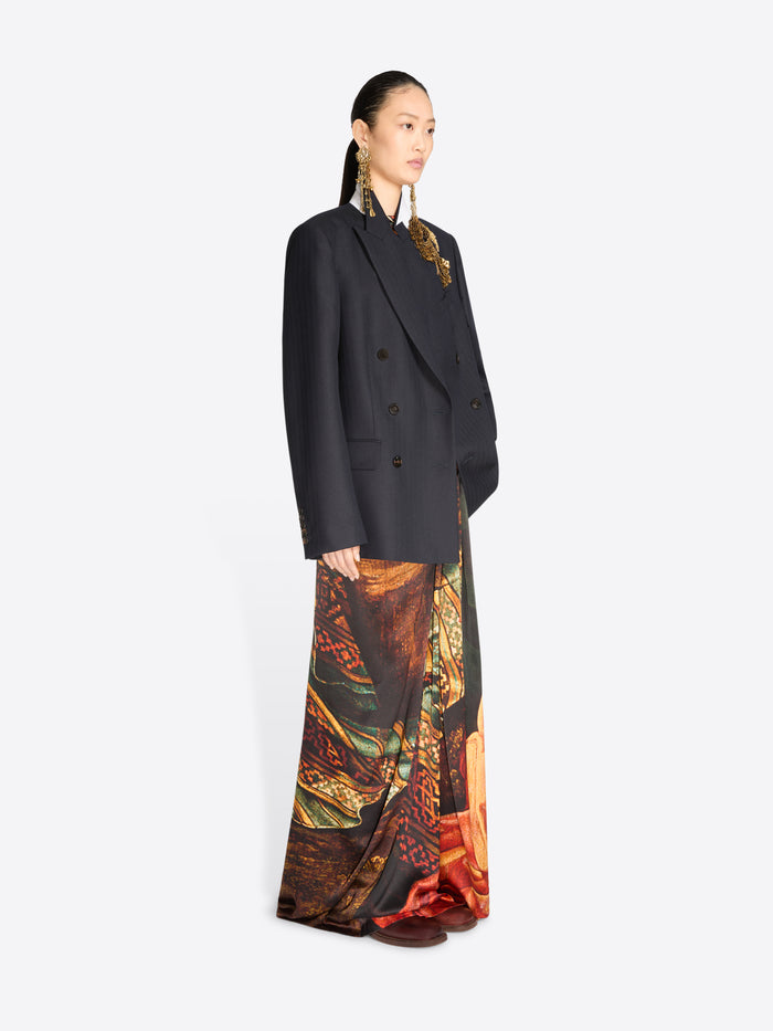 A model wearing a black double-breasted blazer over a long, wide-leg skirt with an intricate multicolor paisley and floral print.