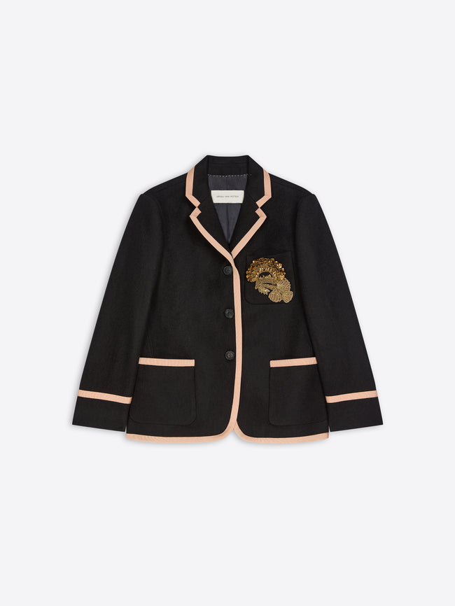 A black blazer jacket featuring light pink piping trim along the collar, front edges, and pocket hems, with a gold embroidered motif on the left chest. 