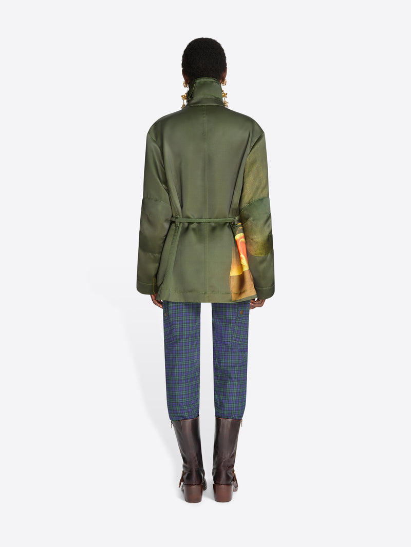 Back view of a model standing against a light gray background wearing a dark green jacket, blue plaid trousers, and dark brown boots.
