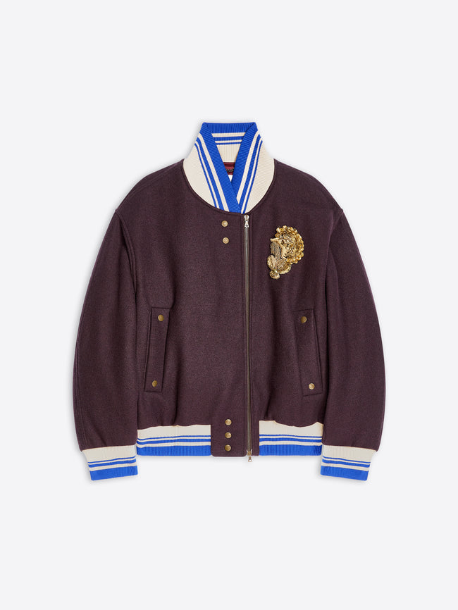 A dark plum varsity-style jacket with cream and blue striped ribbed trim, a gold embroidered detail on the left chest, and a front zipper, shown on a light gray background.