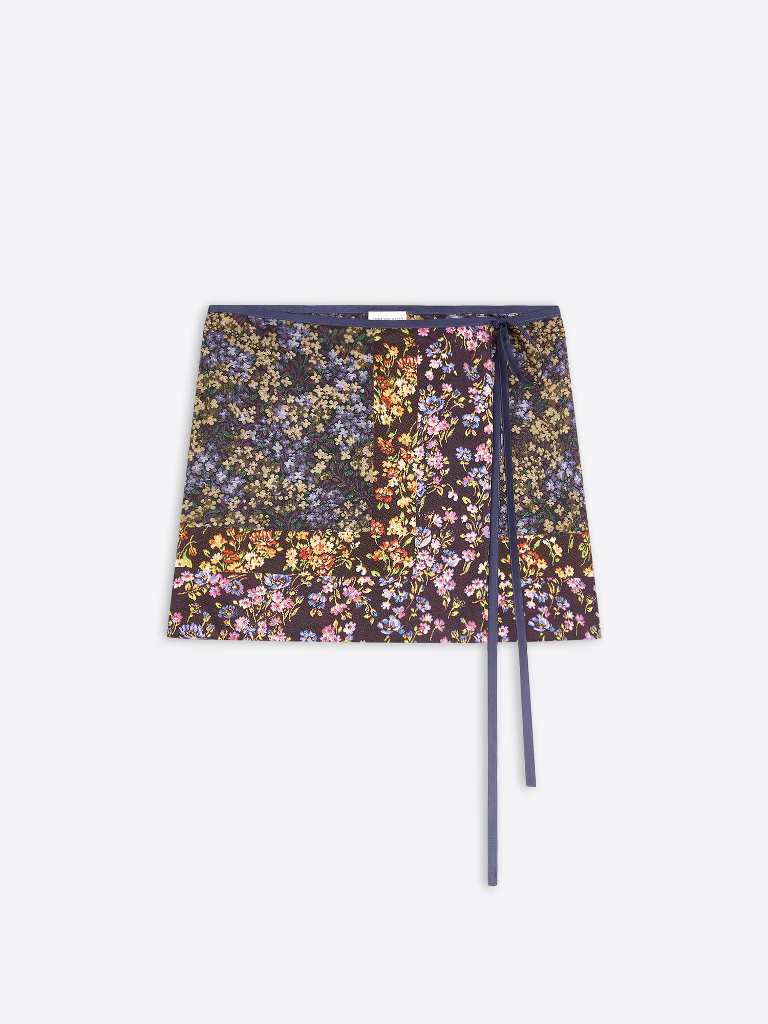 A printed wrap skirt with a dense multicolor floral print on a dark background, featuring a solid navy blue waistband and matching navy blue strings, displayed flat against a light gray background.