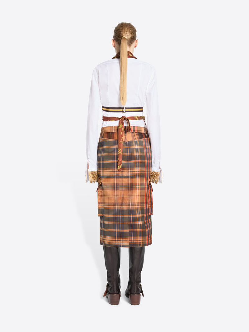 Back view of model standing against a light gray background wearing a white shirt, a rust-orange patterned top with, a brown plaid skirt, and dark brown boots.