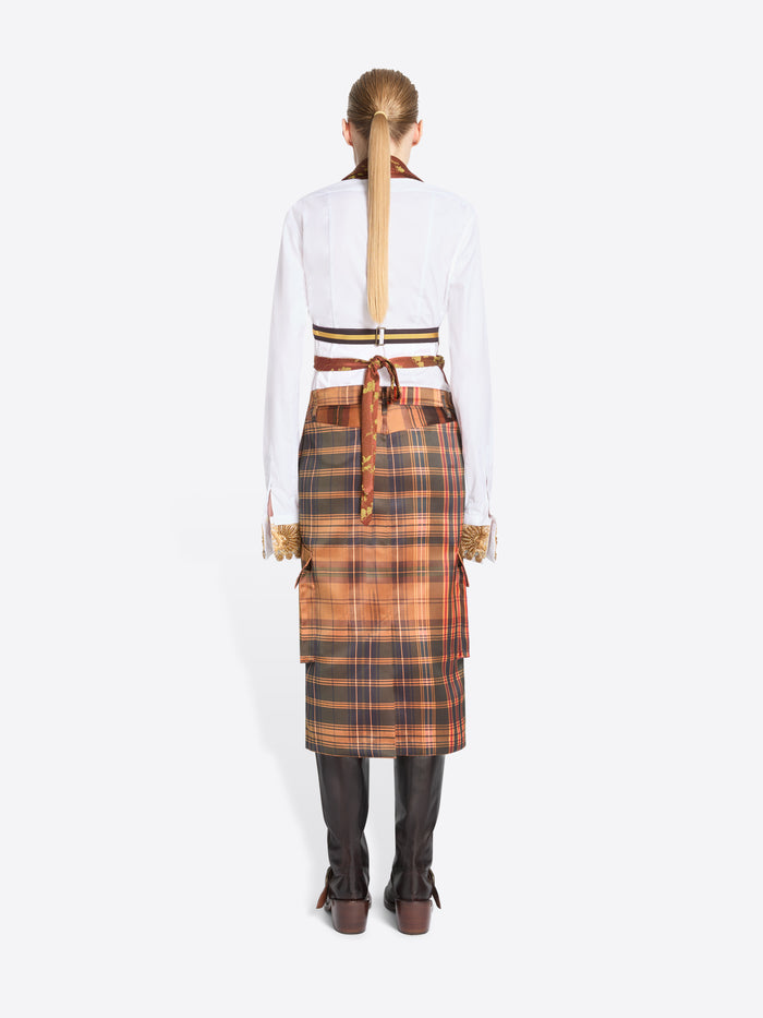 Back view of model standing against a light gray background wearing a white shirt, a rust-orange patterned top with, a brown plaid skirt, and dark brown boots.