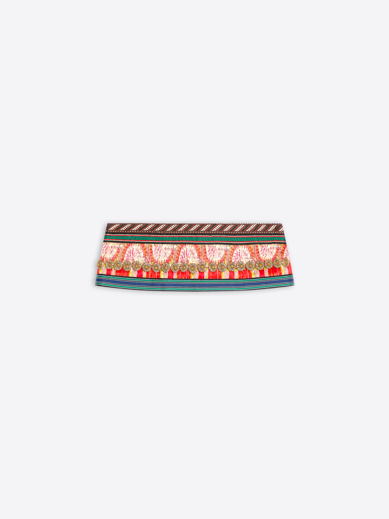 A close-up of a patterned fabric band, likely a belt or waist trim, featuring a red and gold paisley design with a brown geometric border on a light gray background.