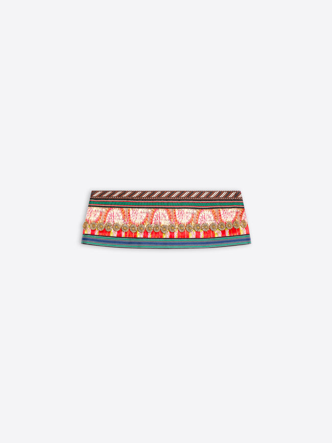 A close-up of a patterned fabric band, likely a belt or waist trim, featuring a red and gold paisley design with a brown geometric border on a light gray background.