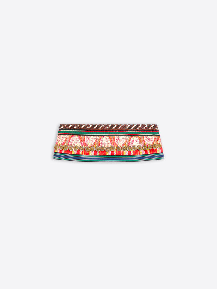 A close-up of a patterned fabric band, likely a belt or waist trim, featuring a red and gold paisley design with a brown geometric border on a light gray background.
