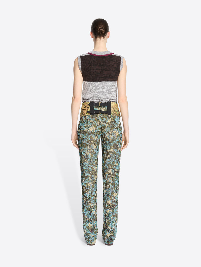 Back view of a model standing against a light gray background wearing a sleeveless knit vest and a gold patterned waistband, paired with matching patterned pants.
