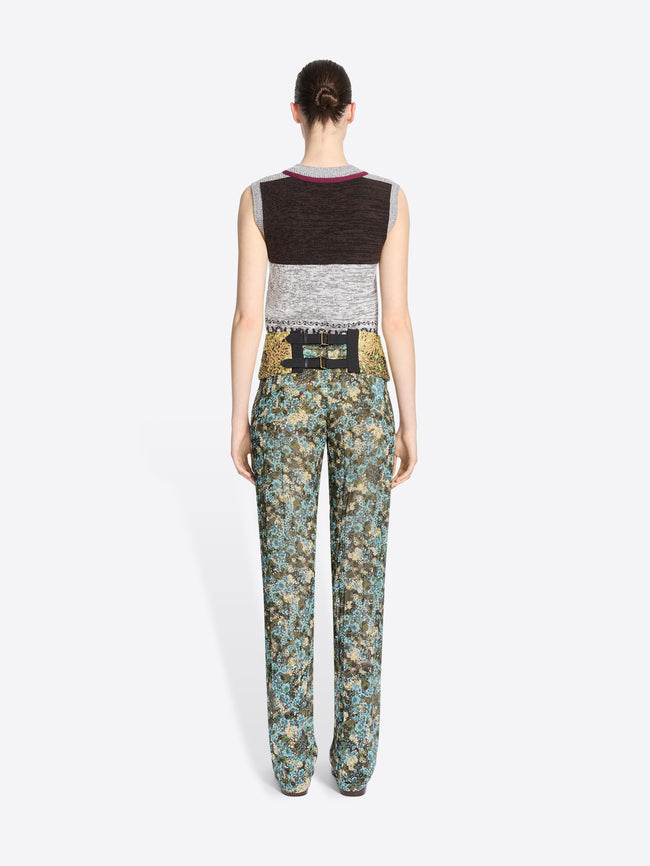 Back view of a model standing against a light gray background wearing a sleeveless knit vest and a gold patterned waistband, paired with matching patterned pants.