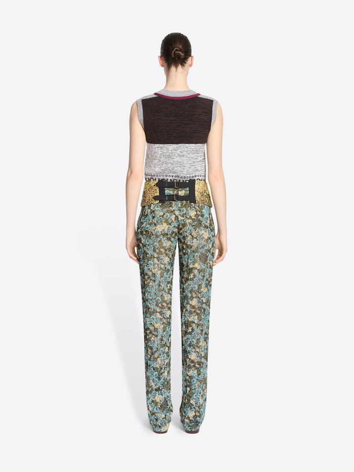 Back view of a model standing against a light gray background wearing a sleeveless knit vest and a gold patterned waistband, paired with matching patterned pants.