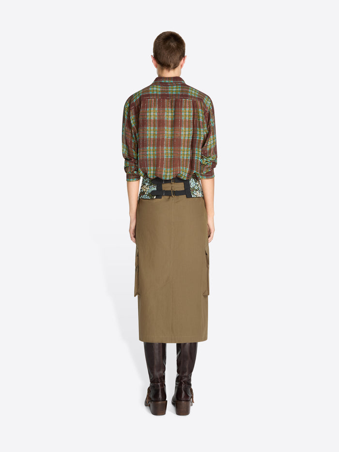 Back view of a model standing against a light gray background wearing a green and red plaid button-up shirt, a patterned waist layer, a khaki cargo-style wrap skirt, and dark brown boots.