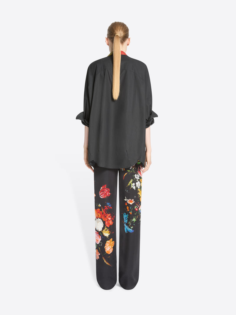 Back view of a model standing against a light gray background wearing a black button-up shirt and matching wide-leg trousers with colorful floral prints.