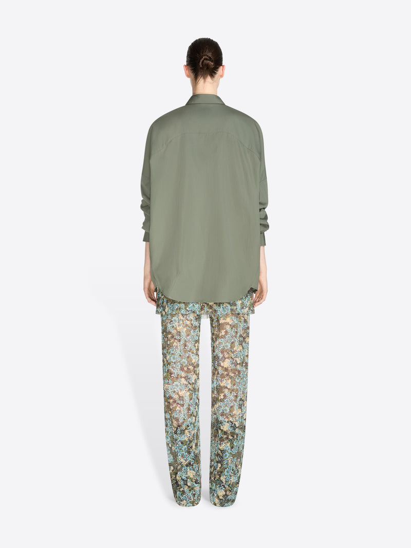 Back view of a model standing against a light gray background wearing an oversized olive green button-up shirt and patterned pants with floral print.