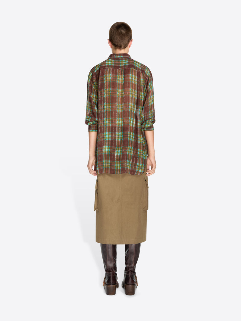 Back view of a model standing against a light gray background wearing a green and brown plaid button-up shirt, a brown cargo-style midi skirt, and dark brown leather boots