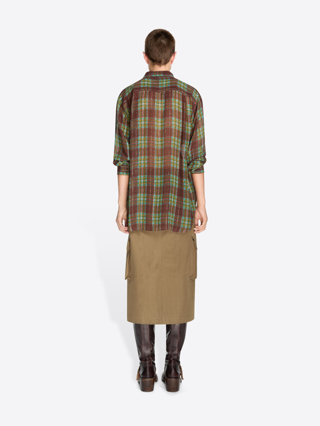 Back view of a model standing against a light gray background wearing a green and brown plaid button-up shirt, a brown cargo-style midi skirt, and dark brown leather boots