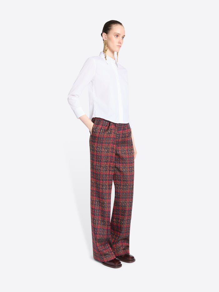 A model stands against a light gray background wearing a white long-sleeve button-up shirt and wide-leg plaid red pants.
