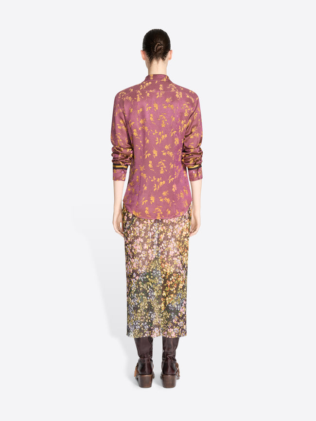 Back view of a model standing against a light gray background wearing a long-sleeve button-up dusty mauve-purple with gold details shirt and a floral midi skirt