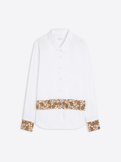 A white long-sleeve button-up shirt with a decorative golden floral lace band across the lower front and matching lace trim on the cuffs, shown against a light gray background.