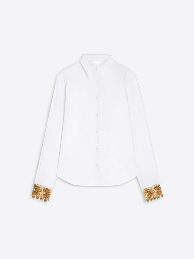 A white long-sleeve button-up shirt with ornate gold sequined cuff details, displayed flat against a light gray background.