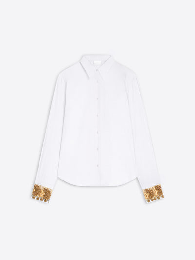 A white long-sleeve button-up shirt with ornate gold sequined cuff details, displayed flat against a light gray background.