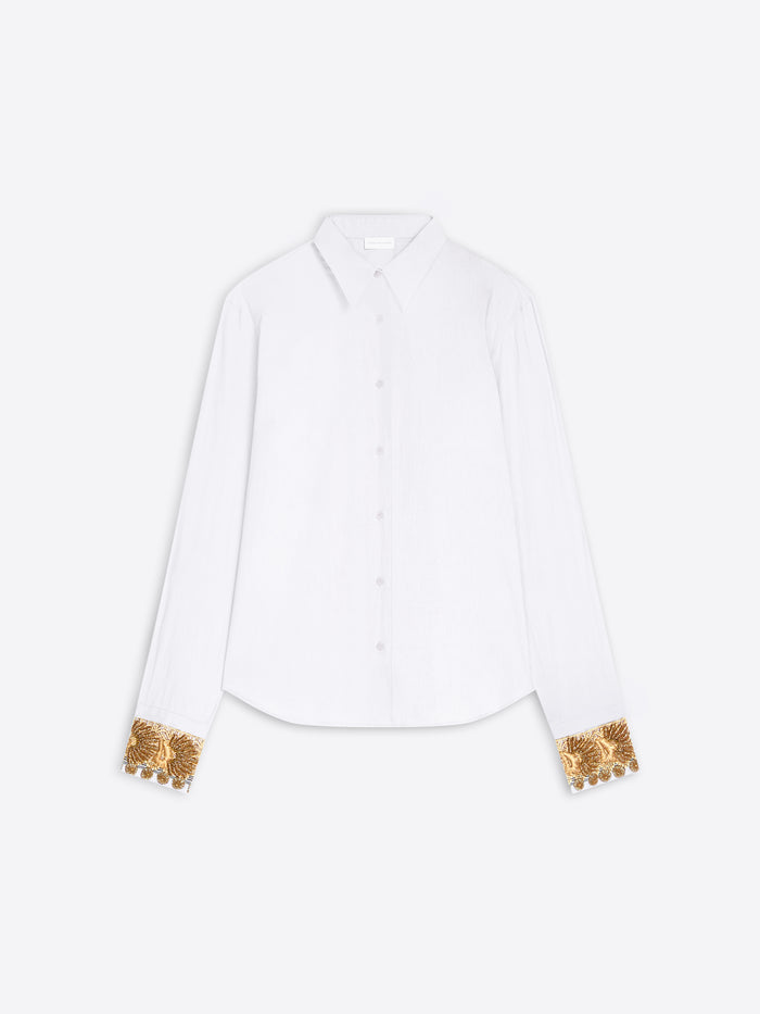 A white long-sleeve button-up shirt with ornate gold sequined cuff details, displayed flat against a light gray background.