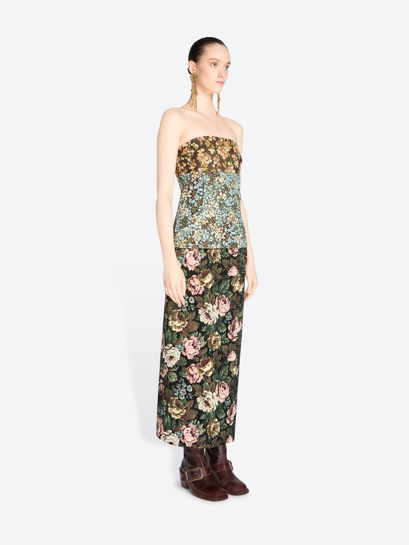 A model wearing a strapless top with a dense floral pattern and matching skirt, paired with dark brown boots against a light gray background.