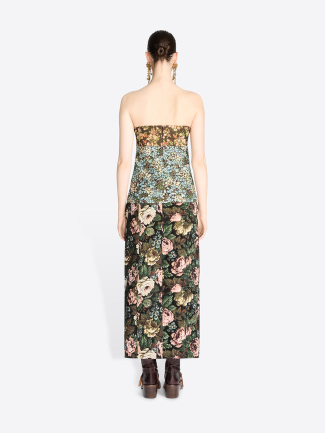 Back view of a model wearing a strapless top with a dense floral pattern and matching skirt, paired with dark brown boots against a light gray background.
