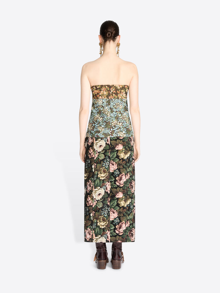 Back view of a model wearing a strapless top with a dense floral pattern and matching skirt, paired with dark brown boots against a light gray background.