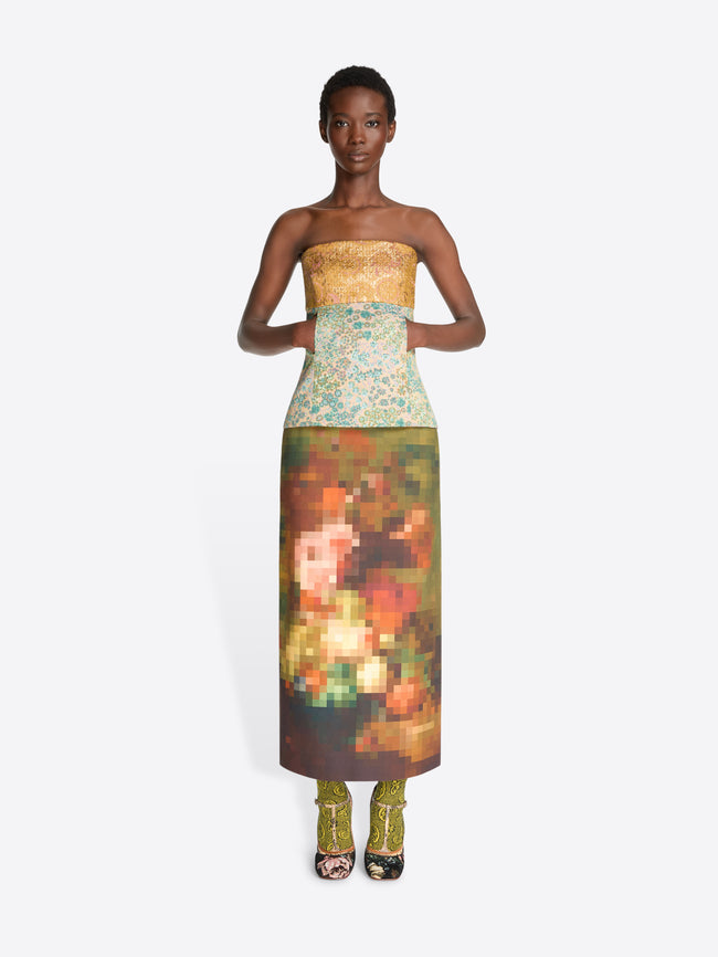 A model wearing a strapless top with a yellow-gold pattern and a multicolor abstract floral print skirt, paired with floral high heels, against a light gray background.