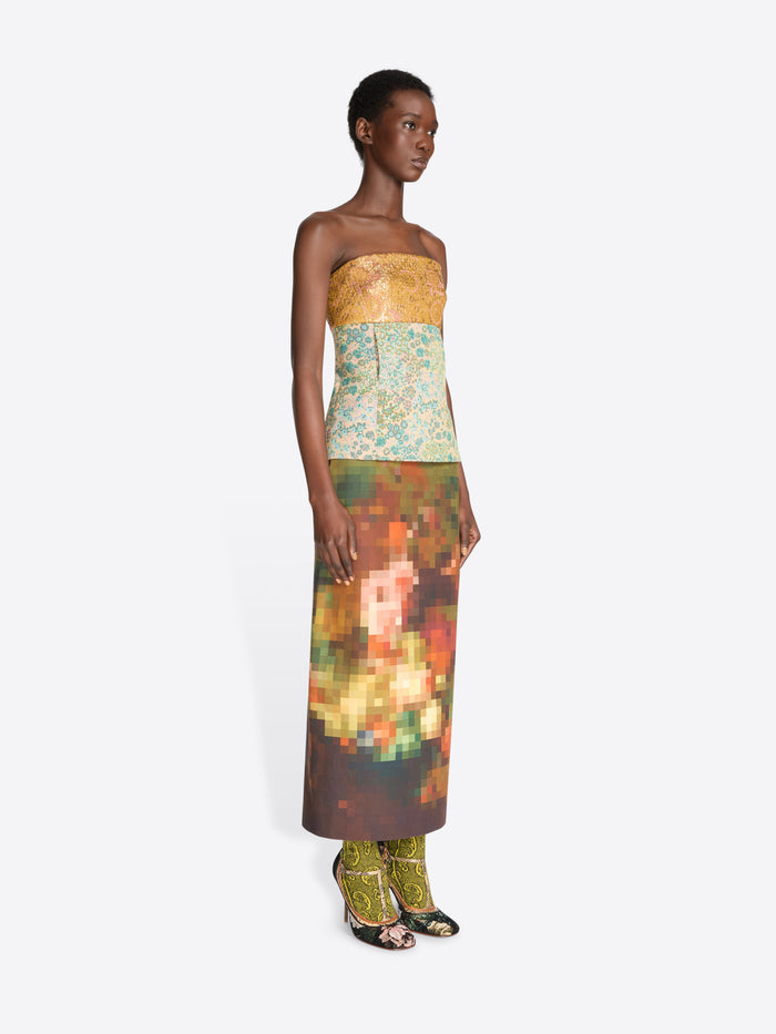 A model wearing a strapless top with a yellow-gold pattern and a multicolor abstract floral print skirt, paired with floral high heels, against a light gray background.