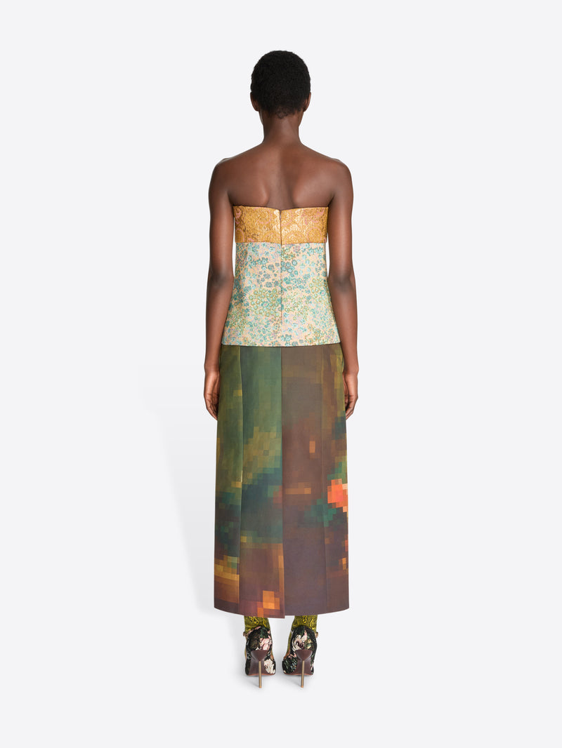 Back view of a model wearing a strapless top with a yellow-gold pattern and a multicolor abstract floral print skirt, paired with floral high heels, against a light gray background.