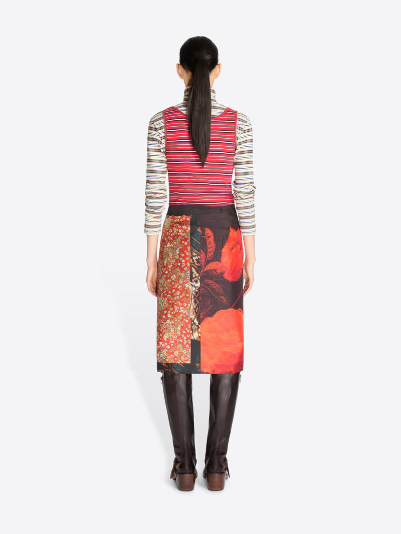 Back view of a model standing against a light gray background wearing a striped red tank top and gray striped turtleneck, a dark wrap skirt with a large red abstract print, and dark brown knee-high boots.