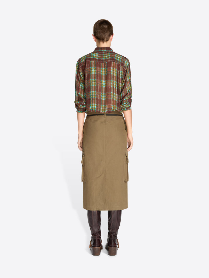 Back view of a model standing against a light gray studio background wearing a green and red plaid button-up shirt tucked into a tan knee-length utility skirt with a black belt, paired with dark brown boots.