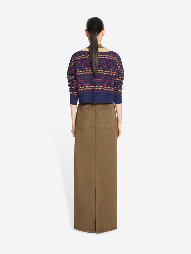 Back view of a model standing against a light gray background wearing a long brown skirt, paired with a patterned knit sweater.