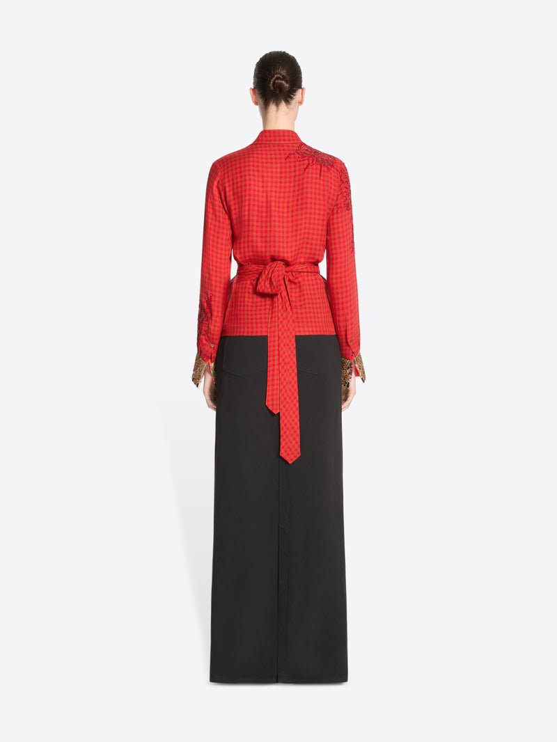 Back view of a model standing against a light gray background wearing a red long-sleeve wrap-style top with gold cuff embellishments and a black maxi skirt with a front slit.