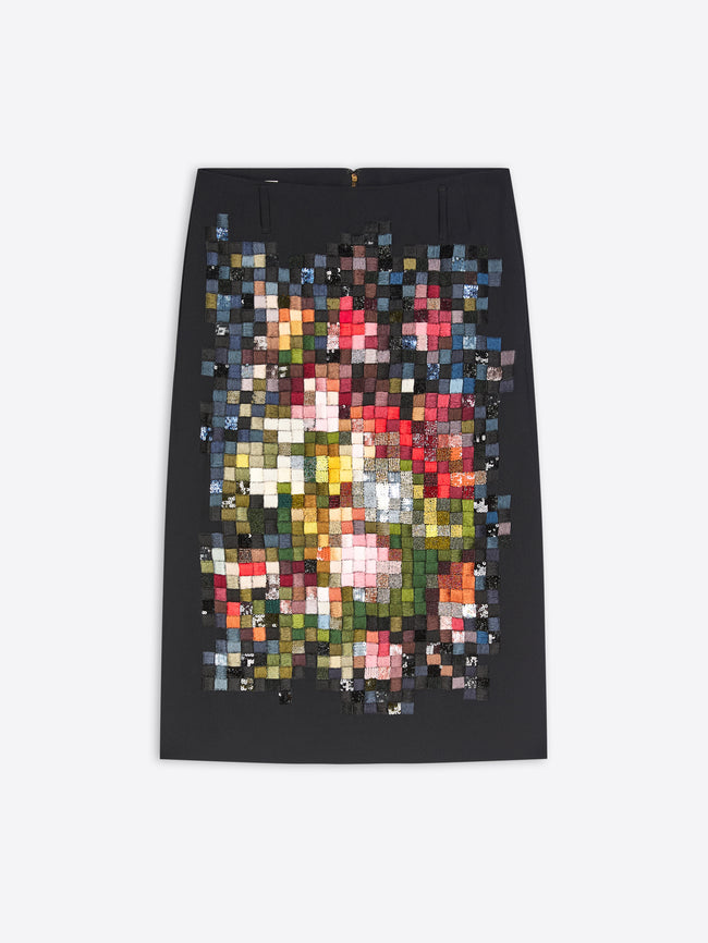 A black pencil skirt featuring a large, colorful pixelated mosaic print of a floral bouquet on the front, displayed flat against a light gray background.