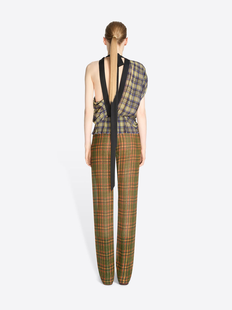 Back view of a model standing against a light gray background wearing a sleeveless asymmetrical plaid top and matching plaid trousers, holding a patterned handbag.
