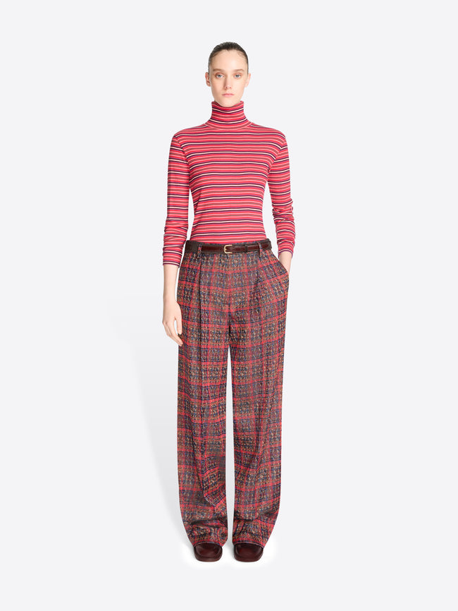 A model stands against a light gray background wearing a red and pink striped long-sleeve turtleneck top with matching red plaid trousers.