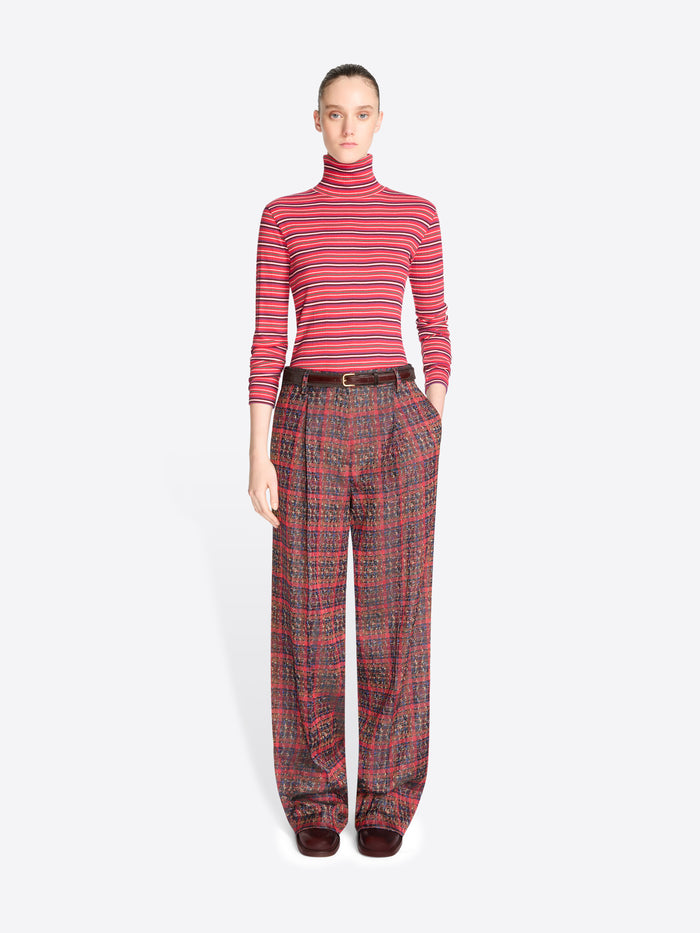 A model stands against a light gray background wearing a red and pink striped long-sleeve turtleneck top with matching red plaid trousers.