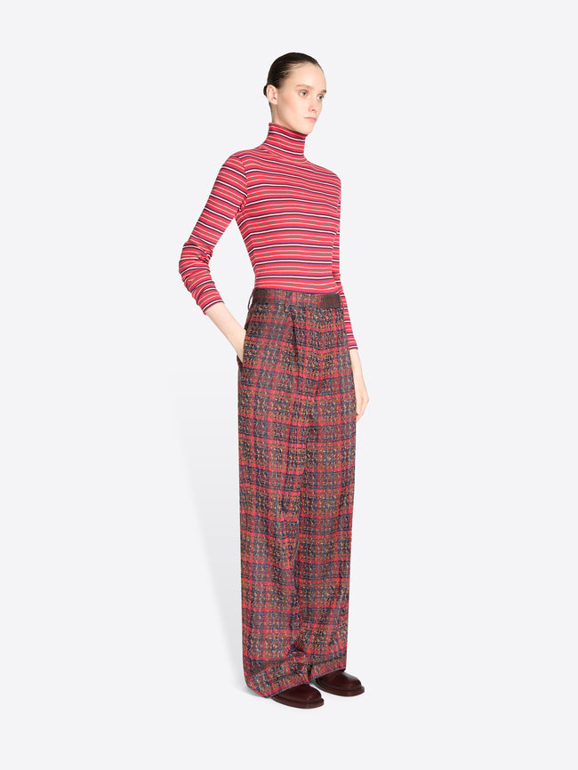 A model stands against a light gray background wearing a red and pink striped long-sleeve turtleneck top with matching red plaid trousers.
