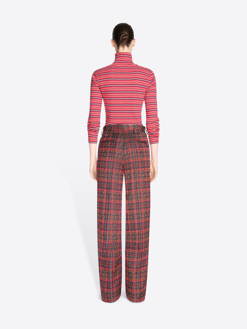 Back view of a model standing against a light gray background wearing a red and pink striped long-sleeve turtleneck top with matching red plaid trousers.