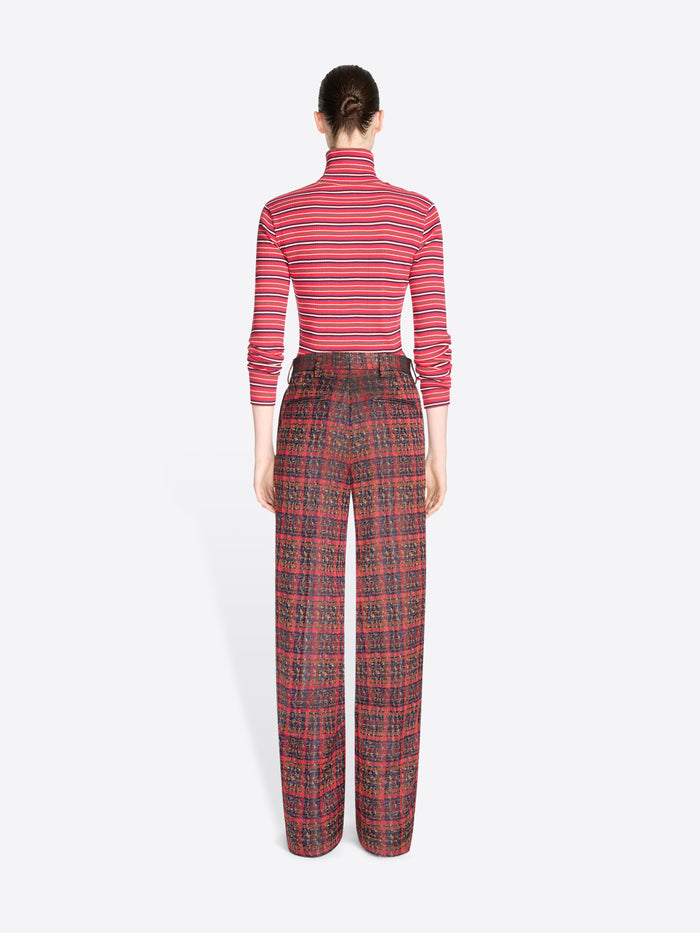 Back view of a model standing against a light gray background wearing a red and pink striped long-sleeve turtleneck top with matching red plaid trousers.