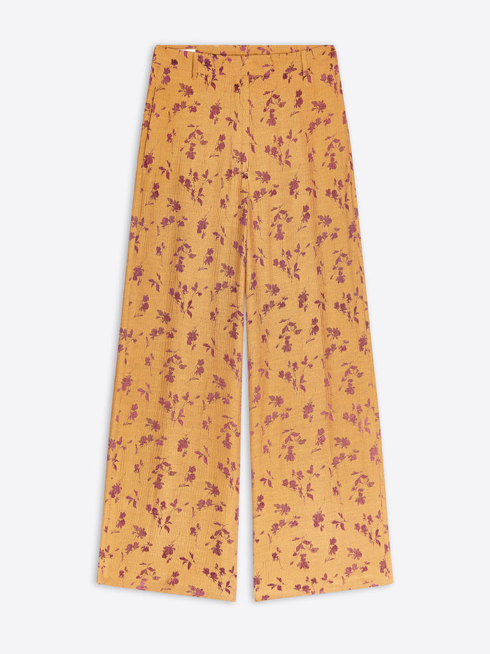 Ochre-colored wide-leg trousers with a small purple floral pattern, shown flat against a light gray background.