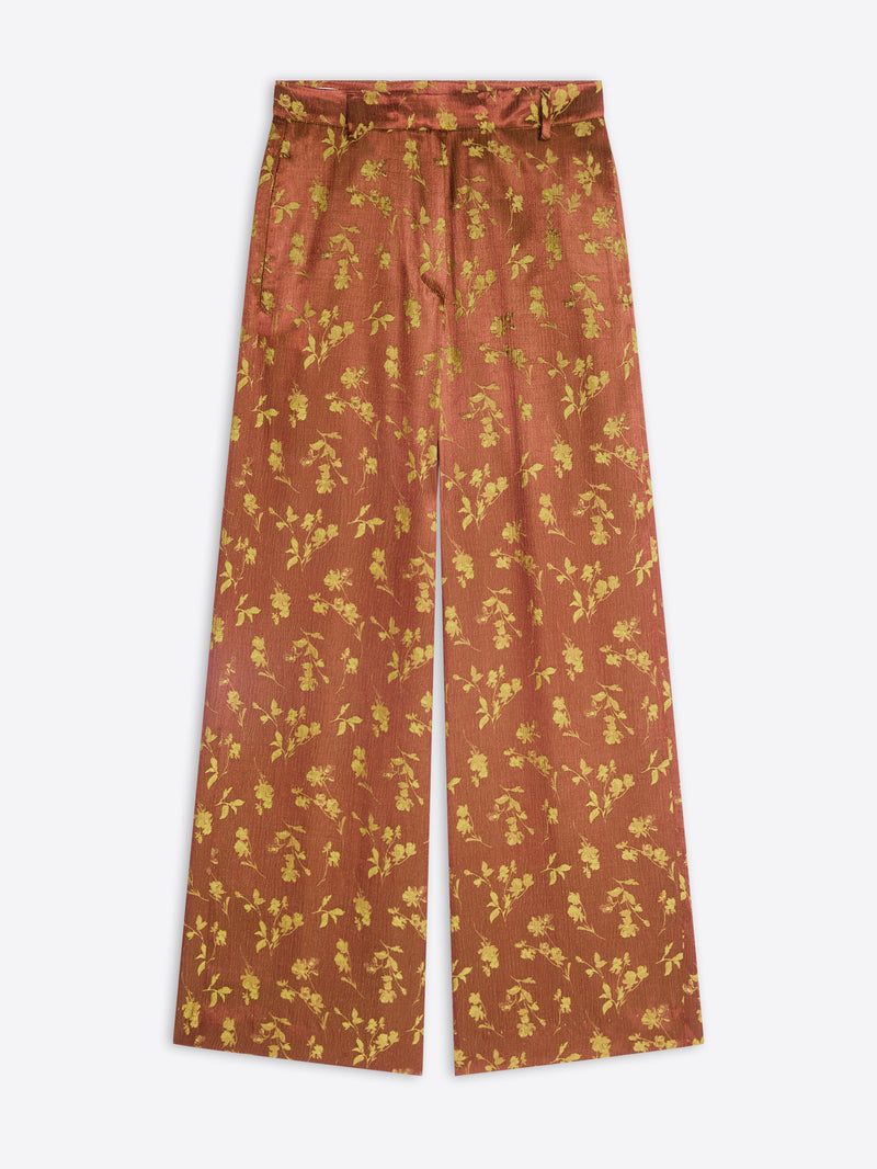 A pair of wide-leg trousers in a rust-orange color with a yellow floral pattern, shown flat against a light gray background.
