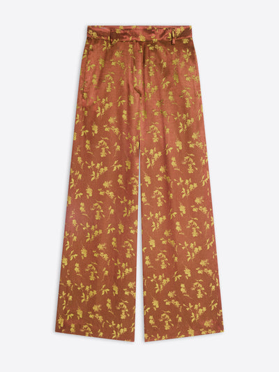 A pair of wide-leg trousers in a rust-orange color with a yellow floral pattern, shown flat against a light gray background.