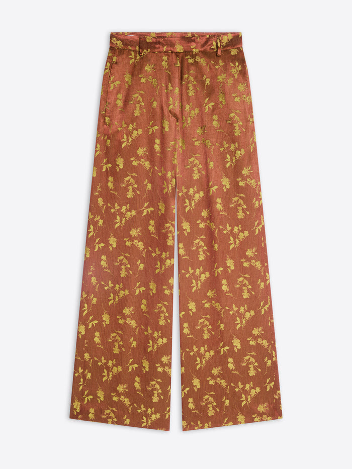 A pair of wide-leg trousers in a rust-orange color with a yellow floral pattern, shown flat against a light gray background.