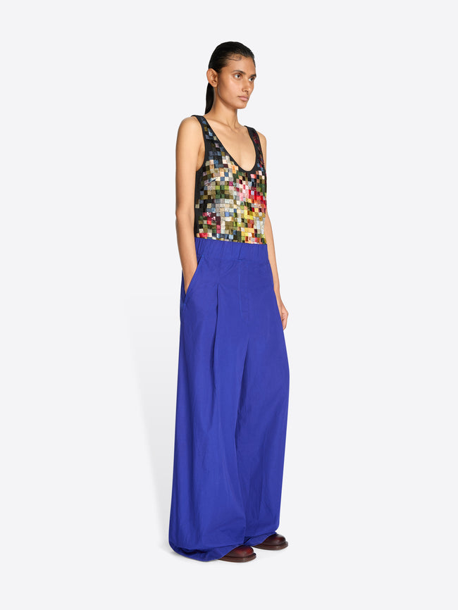 Back view of a model standing against a light gray background wearing a sleeveless top with a multicolor pixelated pattern and a gold textured waistband, paired with wide-leg royal blue pants.
