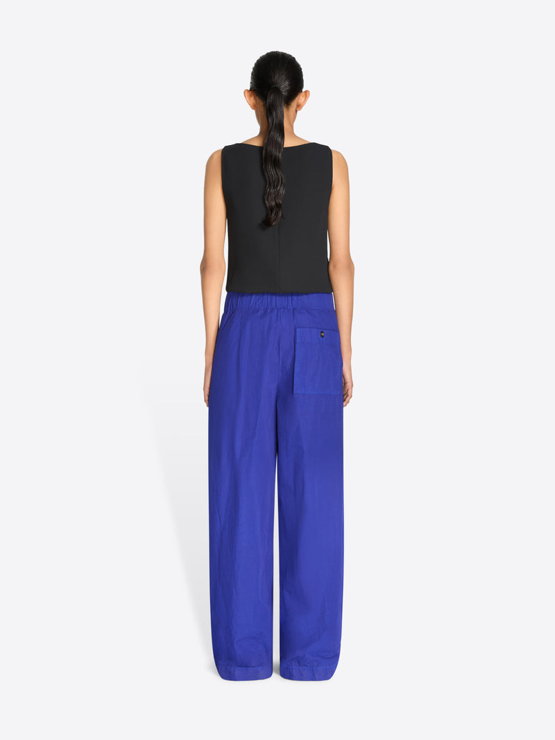 Back view of a model stands against a light gray background wearing a sleeveless top with a multicolor pixelated pattern and a gold textured waistband, paired with wide-leg royal blue pants.