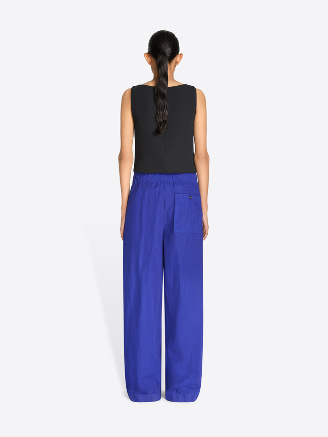 Back view of a model stands against a light gray background wearing a sleeveless top with a multicolor pixelated pattern and a gold textured waistband, paired with wide-leg royal blue pants.
